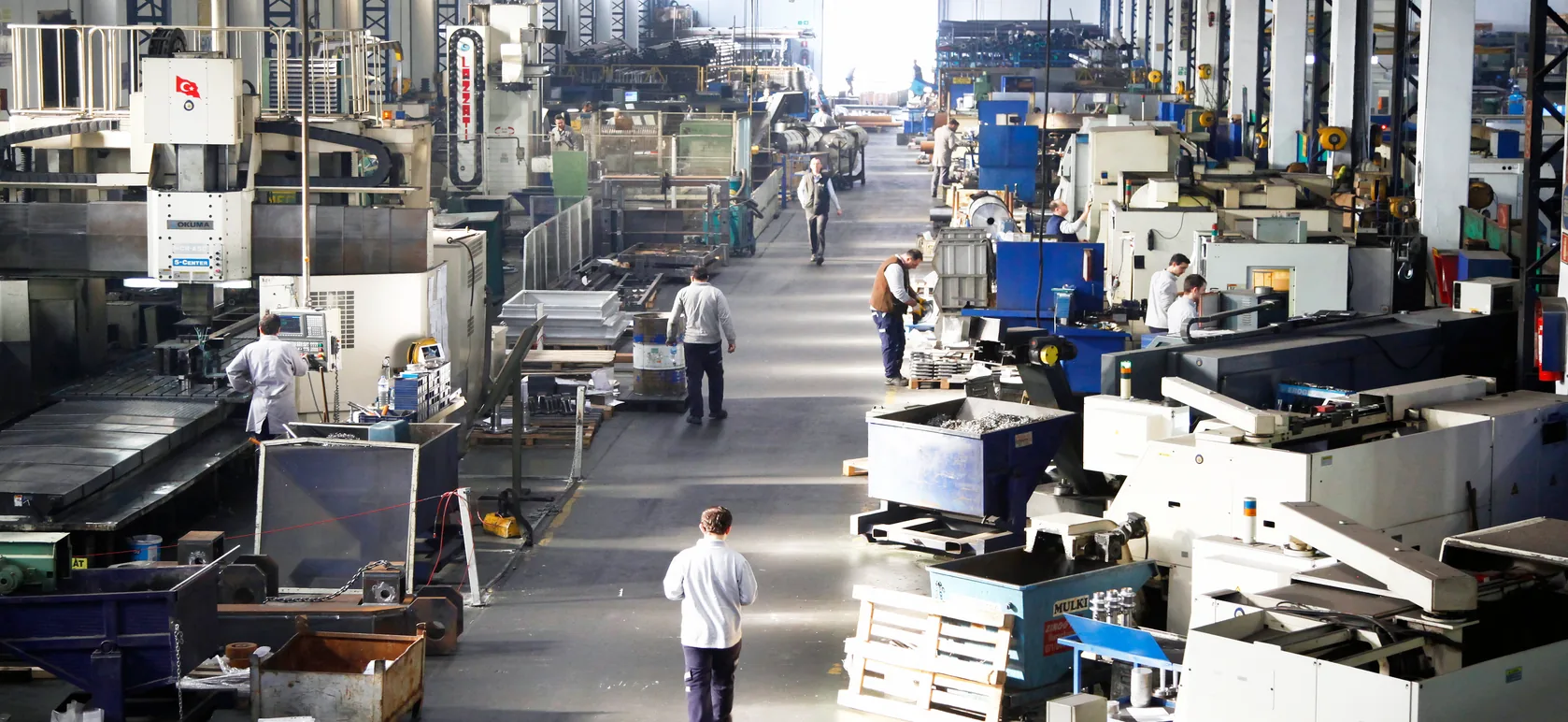 A busy machine shop floor with rows of CNC machines and workers at them